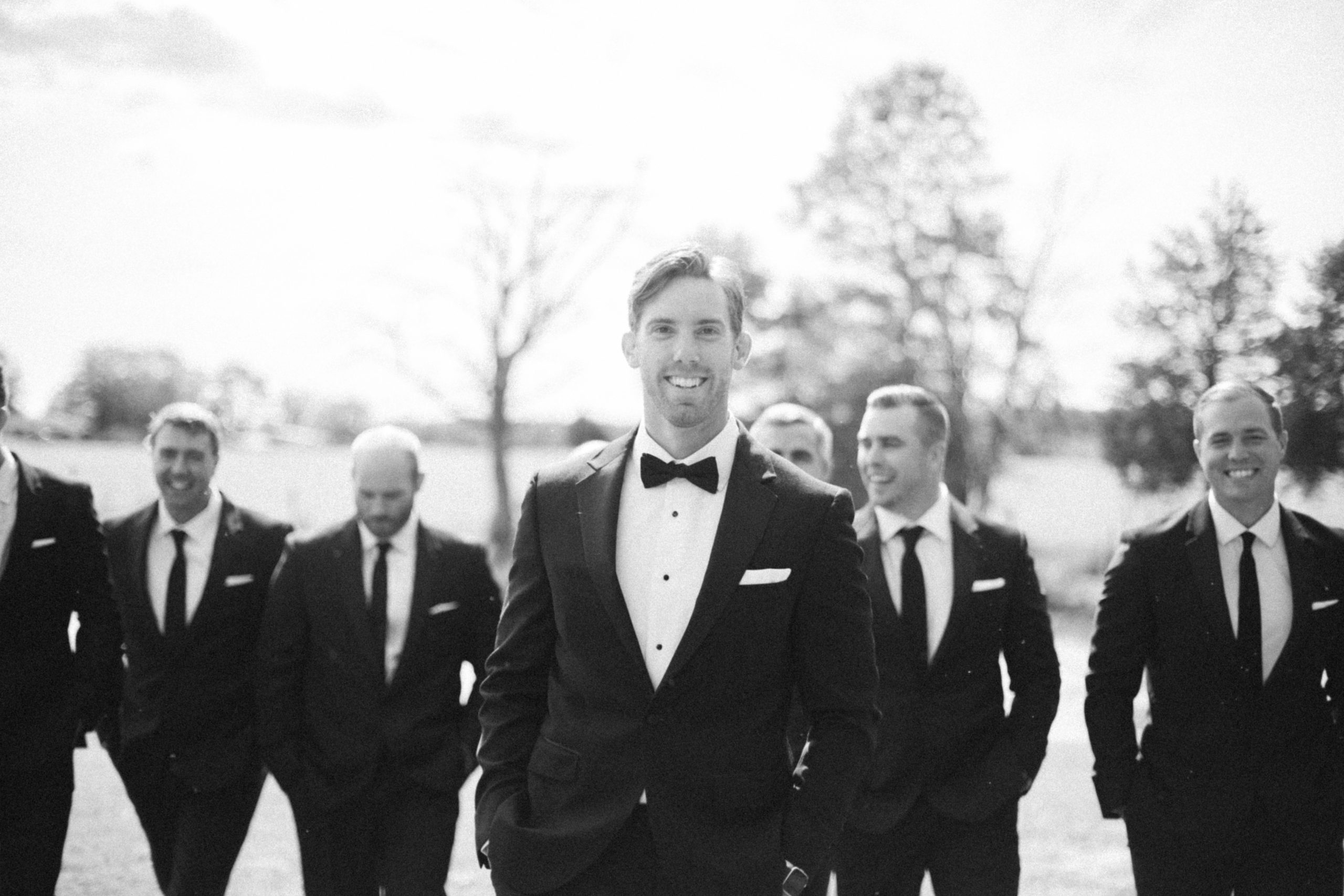 groom walking with his groomsmen in a field and smiling at the camera