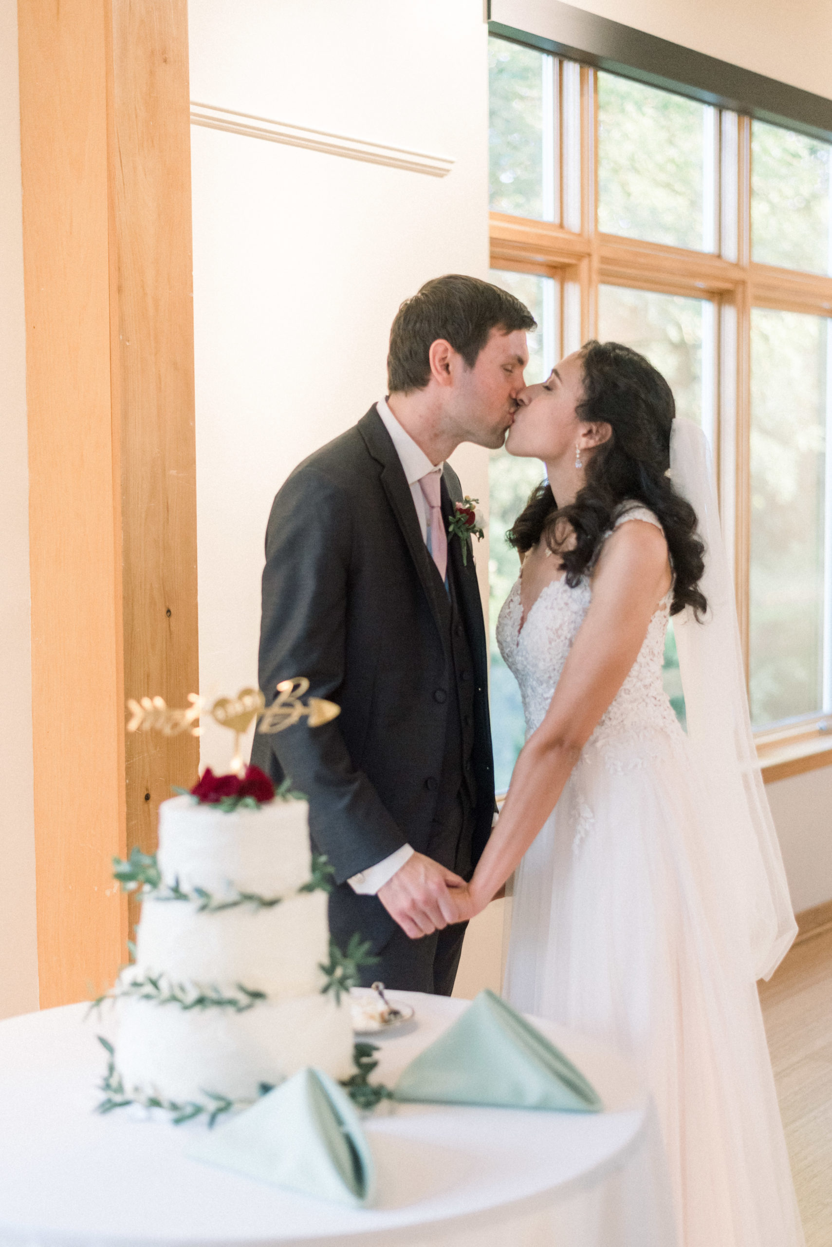 bride and groom kissing in front of cake at chic Howard county conservancy wedding reception