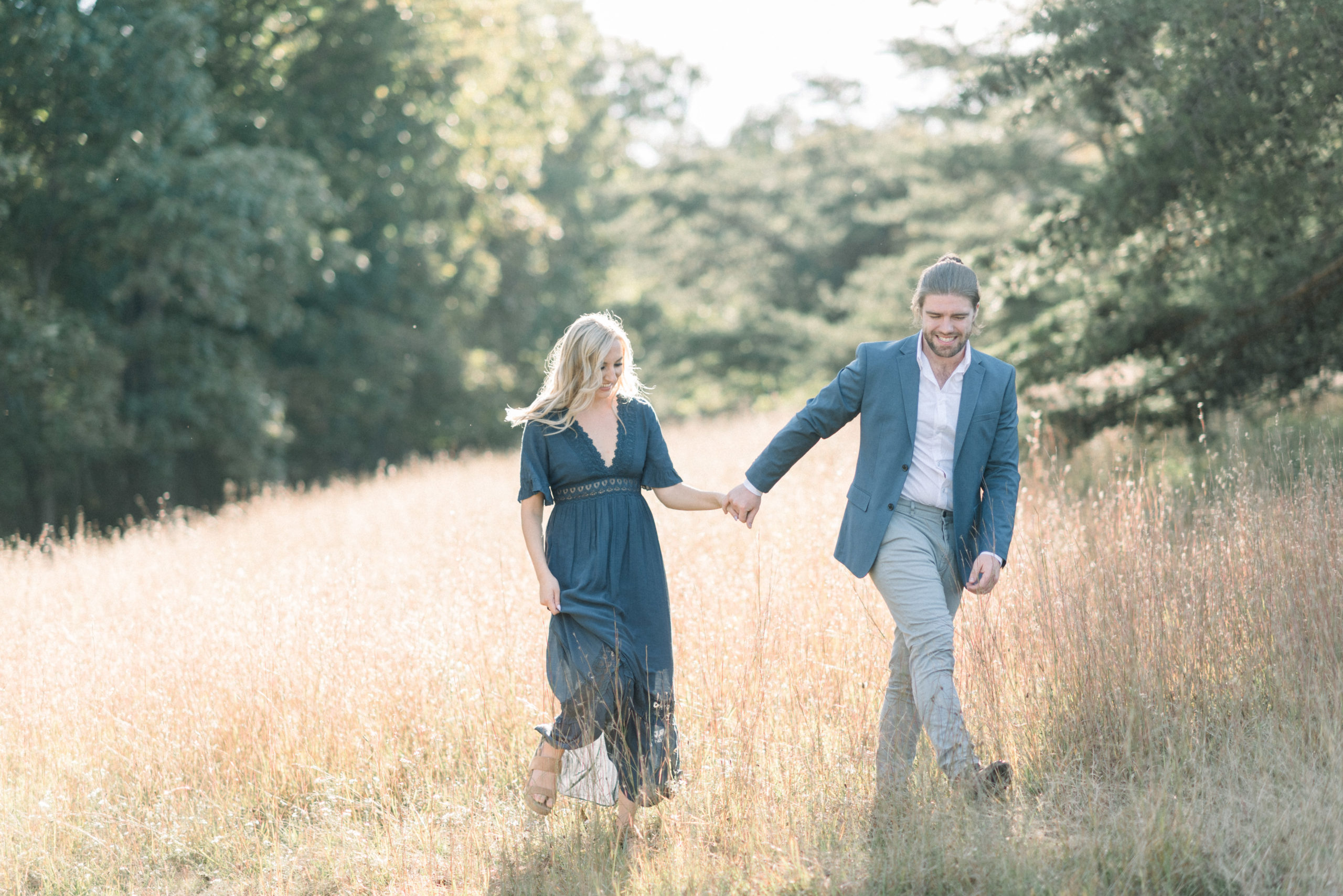man and woman holding hands walking through field of golden grass