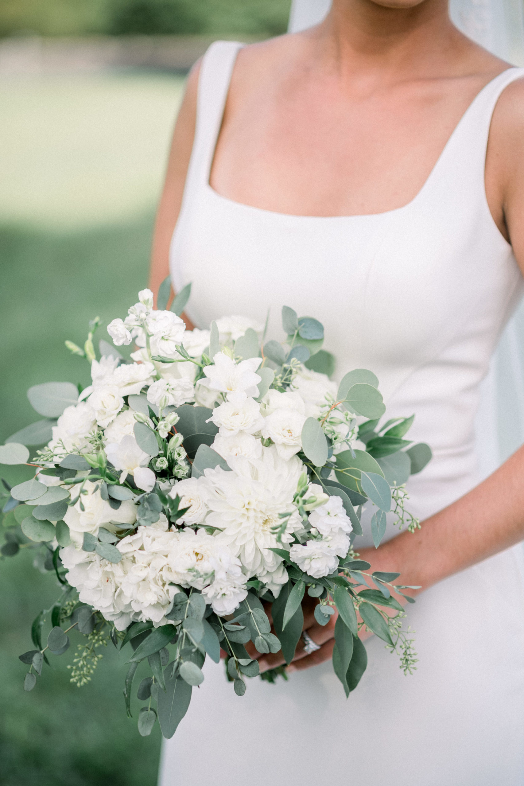 bride holding a white rose and greenery bouquet for her outside wedding