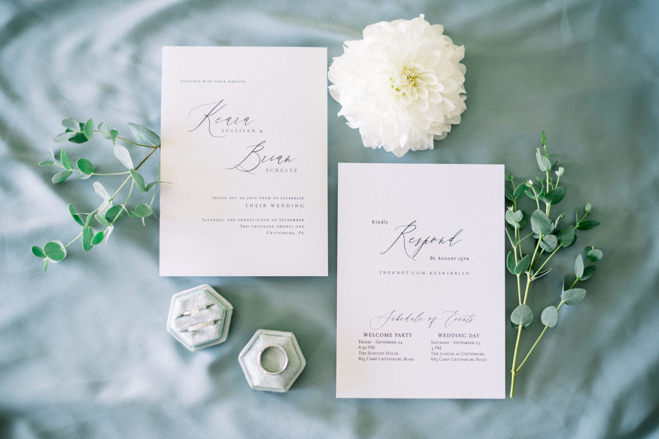 flatlay of wedding invitations and florals and wedding rings on a light blue fabric