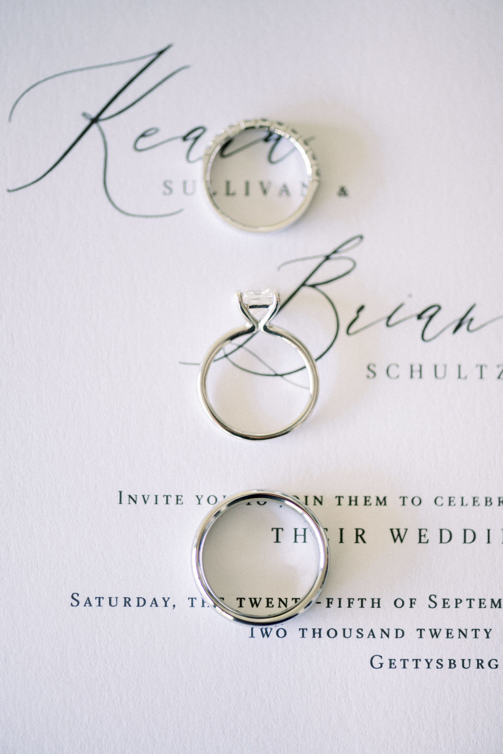 wedding rings and engagement rings laying on a wedding invitation