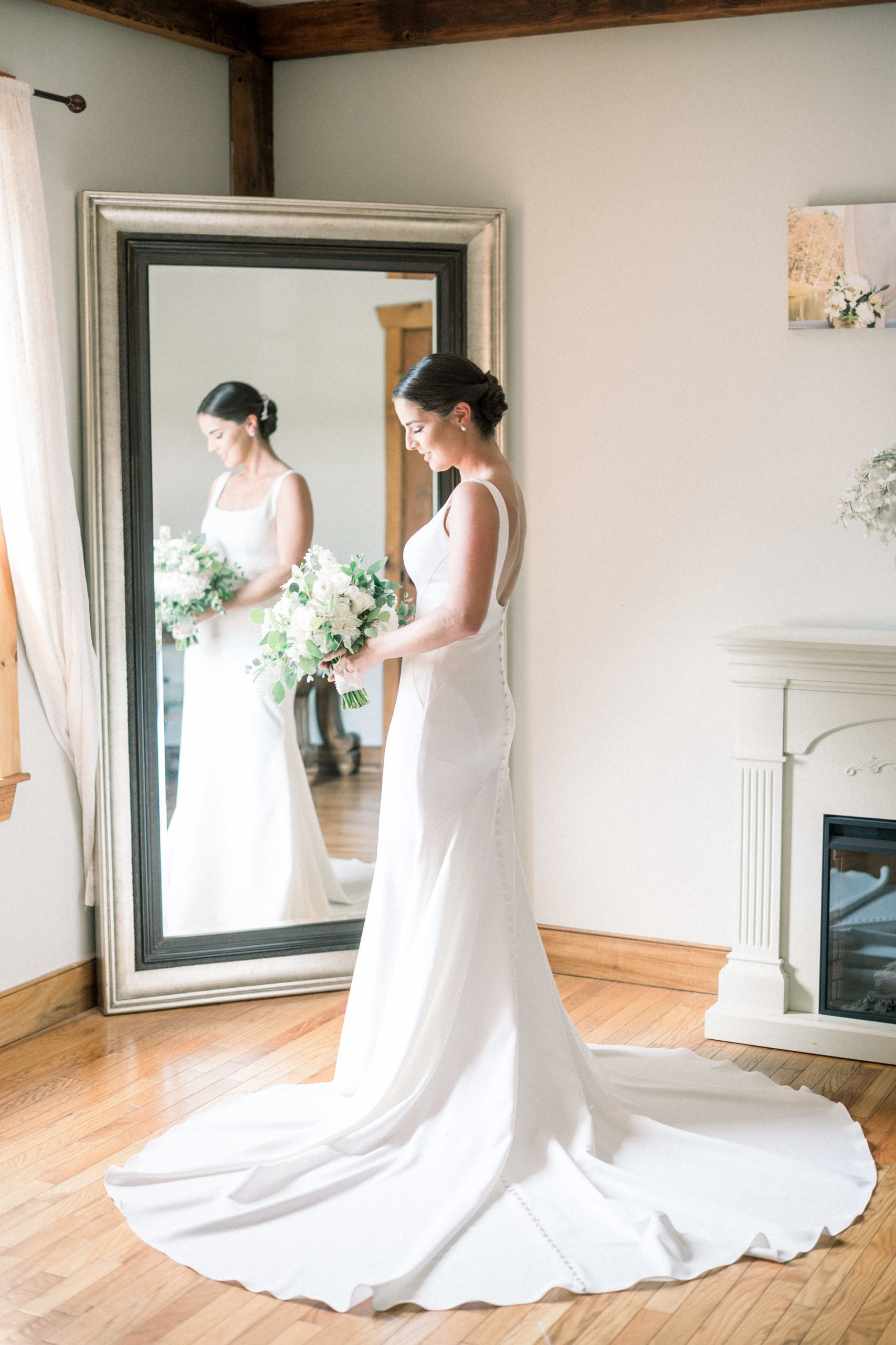 bride standing in front fo a full length mirror holding her wedding bouquet in front of a window