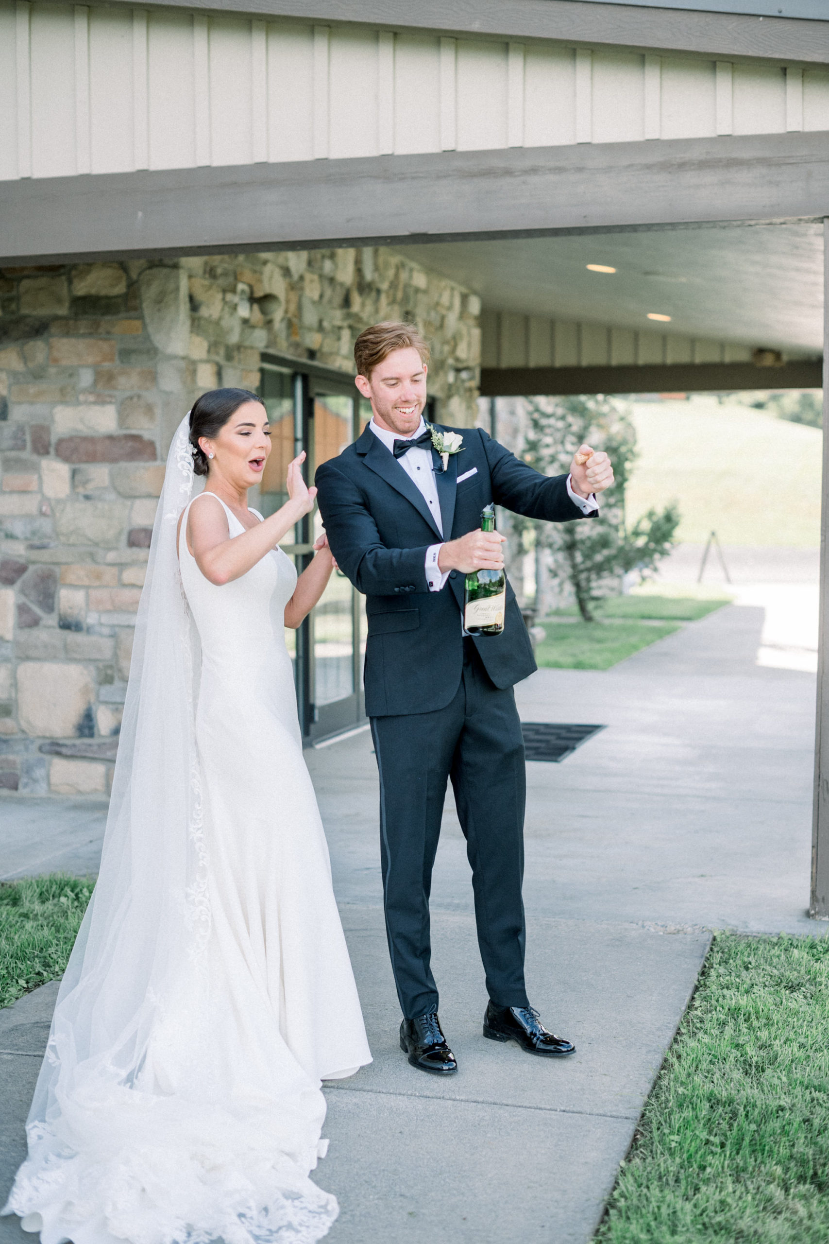 groom pops a bottle of champagne outside of their wedding venue in celebration