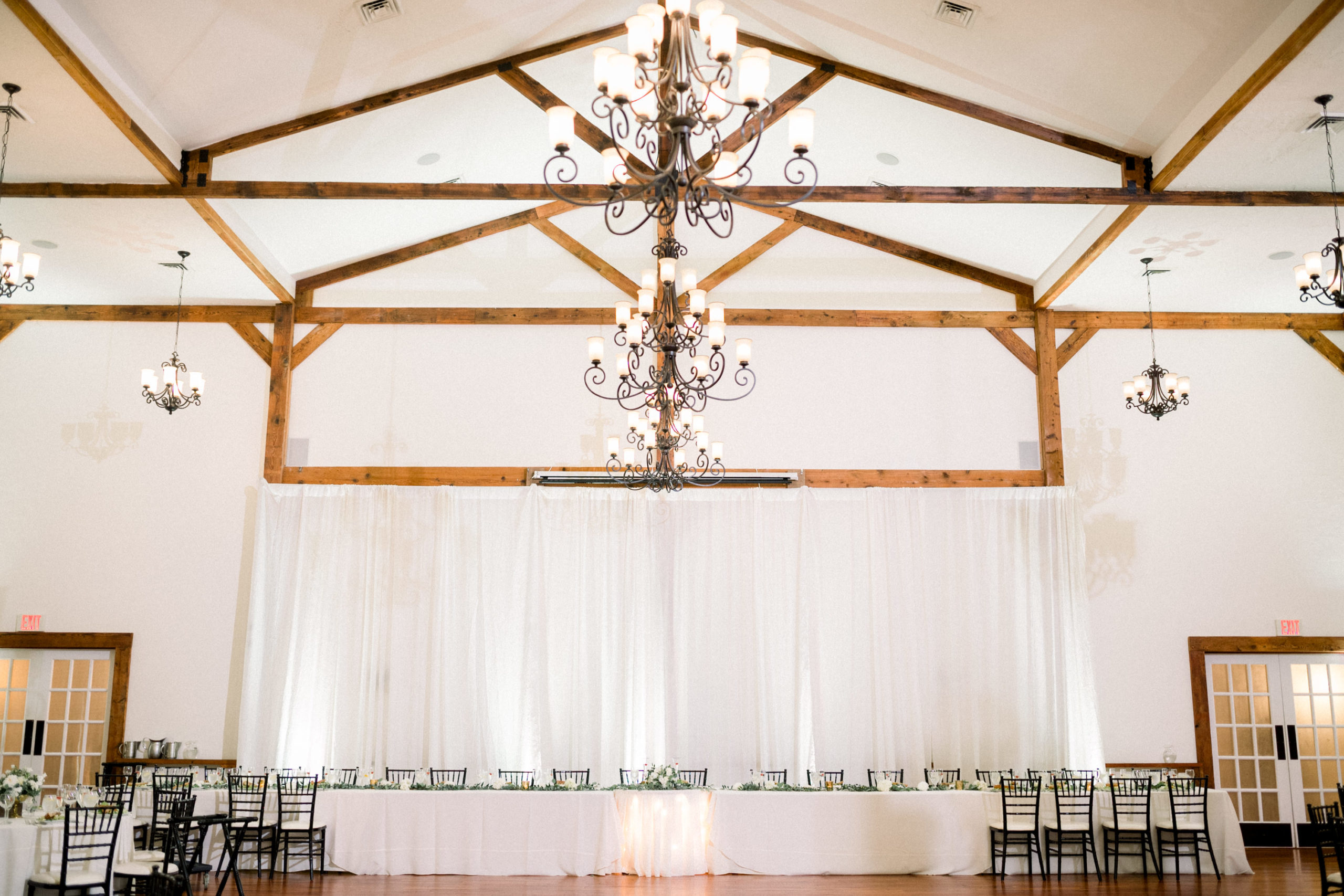 reception hall with iron chandeliers and exposes wooden beams with white drapes 