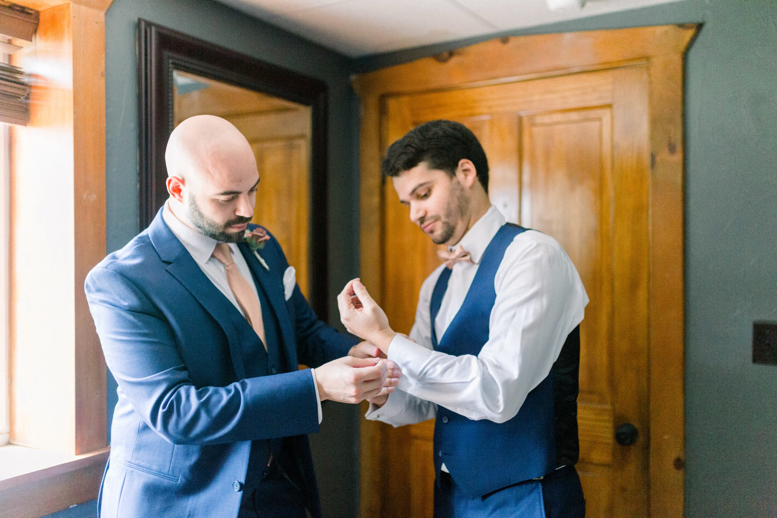 groomsmen wearing navy suit helping groom with sleeves on shirt