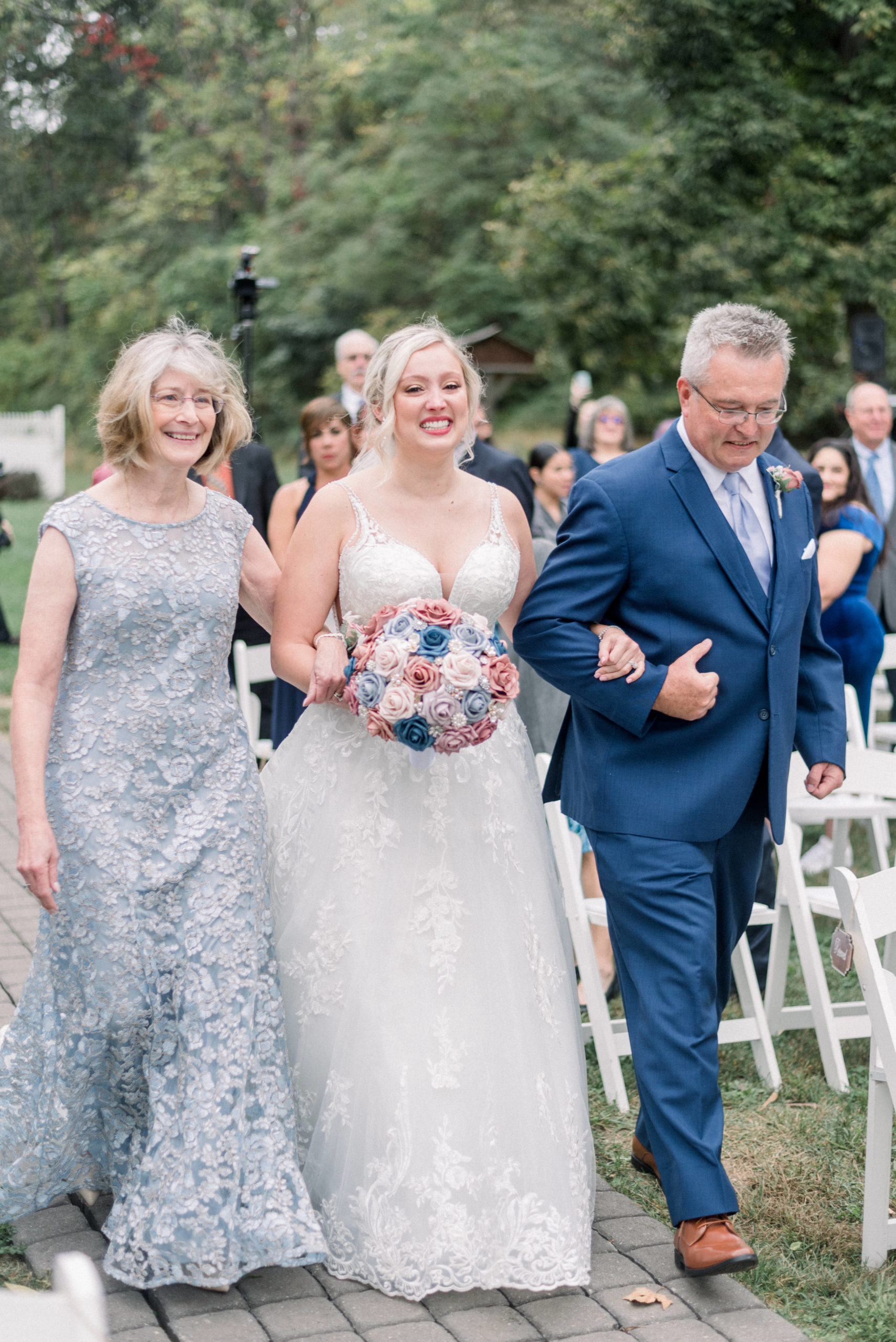 bride smiling and crying while being walked down aisle by mother and father