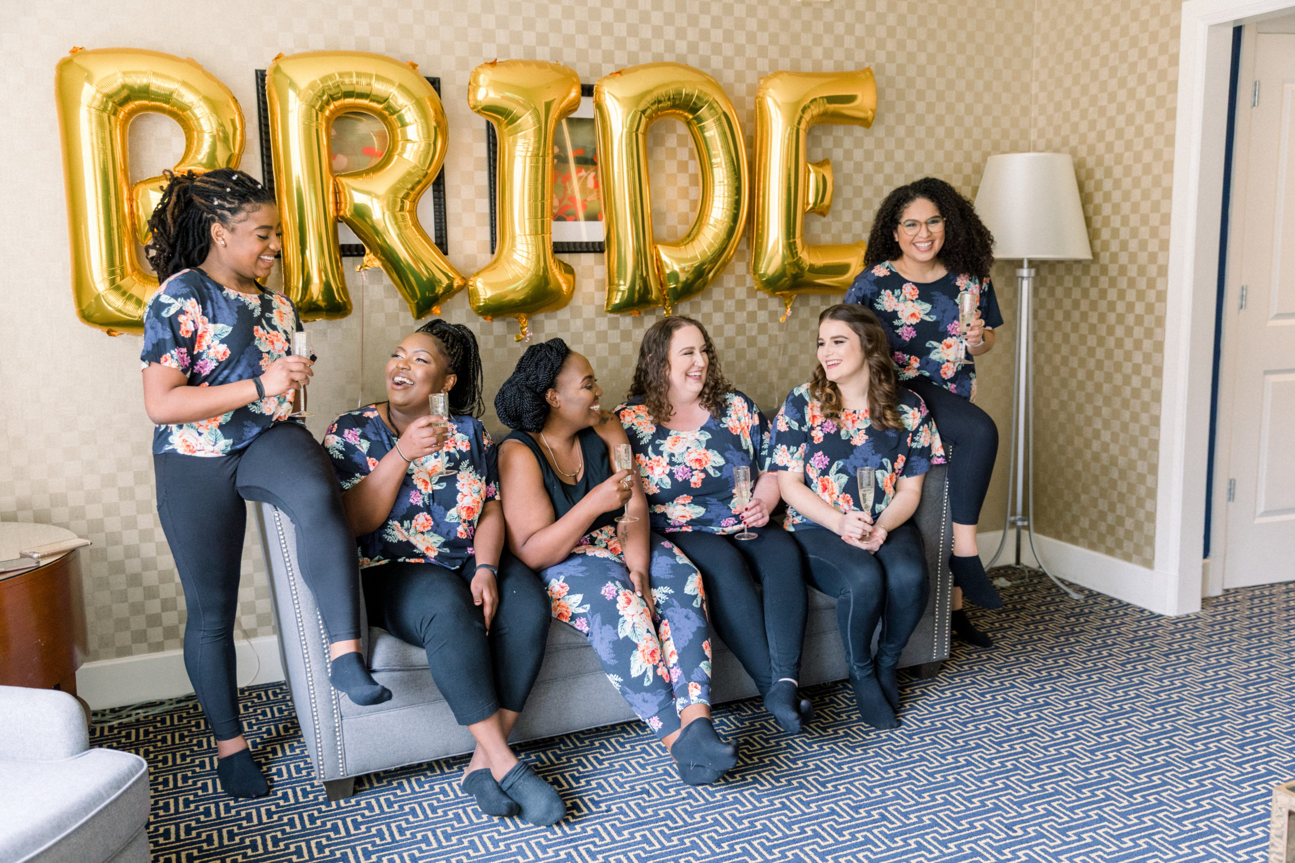 bride sitting on couch with bridesmaids wearing matching shirts before Romantic Fall Baltimore Wedding